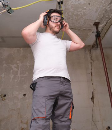 Young builder wearing hearing protection and safety glasses at a construction site. Safety at work. Young builder wearing hearing protection and safety glasses at a construction site. Safety at work.